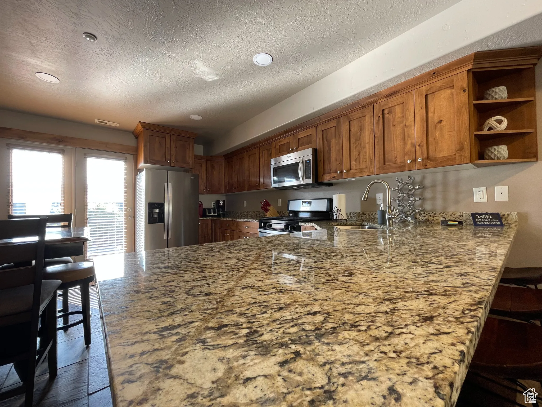 Kitchen with a peninsula, open shelves, a breakfast bar, light stone countertops, and stainless steel appliances