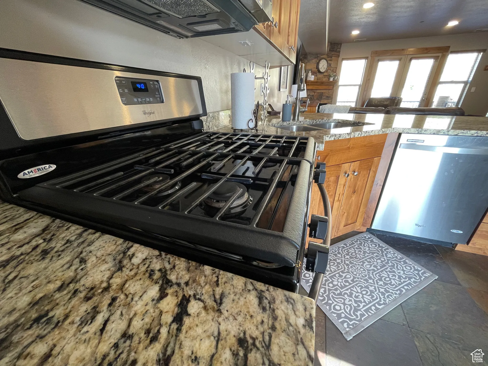 Kitchen with stainless steel appliances, brown cabinets, light stone countertops, and stone tile floors
