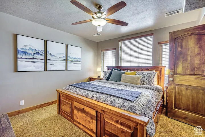 Bedroom with a textured ceiling, light colored carpet, and ceiling fan