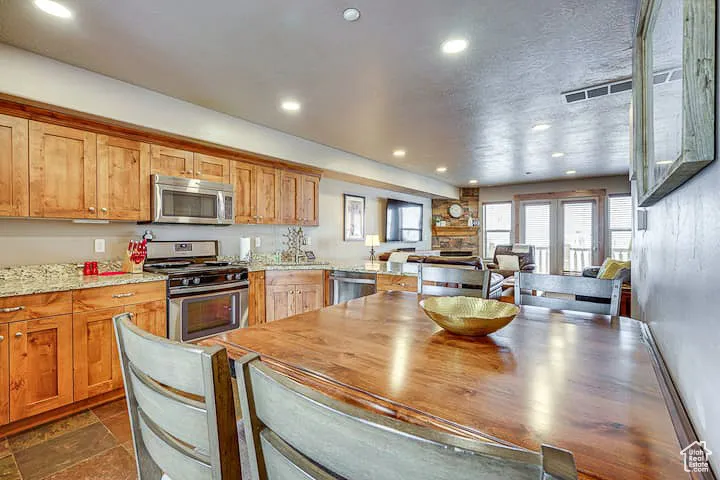 Kitchen featuring stainless steel appliances, light stone countertops, recessed lighting, a peninsula, and brown cabinetry
