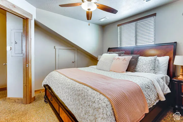 Carpeted bedroom with ceiling fan, electric panel, and a textured ceiling