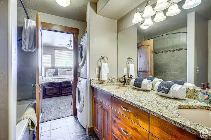 Ensuite bathroom with double vanity, estacked washer and dryer, a textured ceiling, ceiling fan, and shower / tub combo