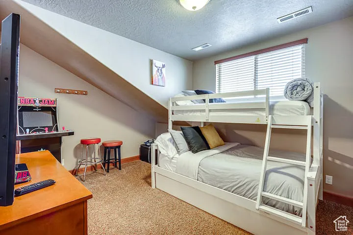Bedroom featuring light colored carpet, a textured ceiling, and a desk