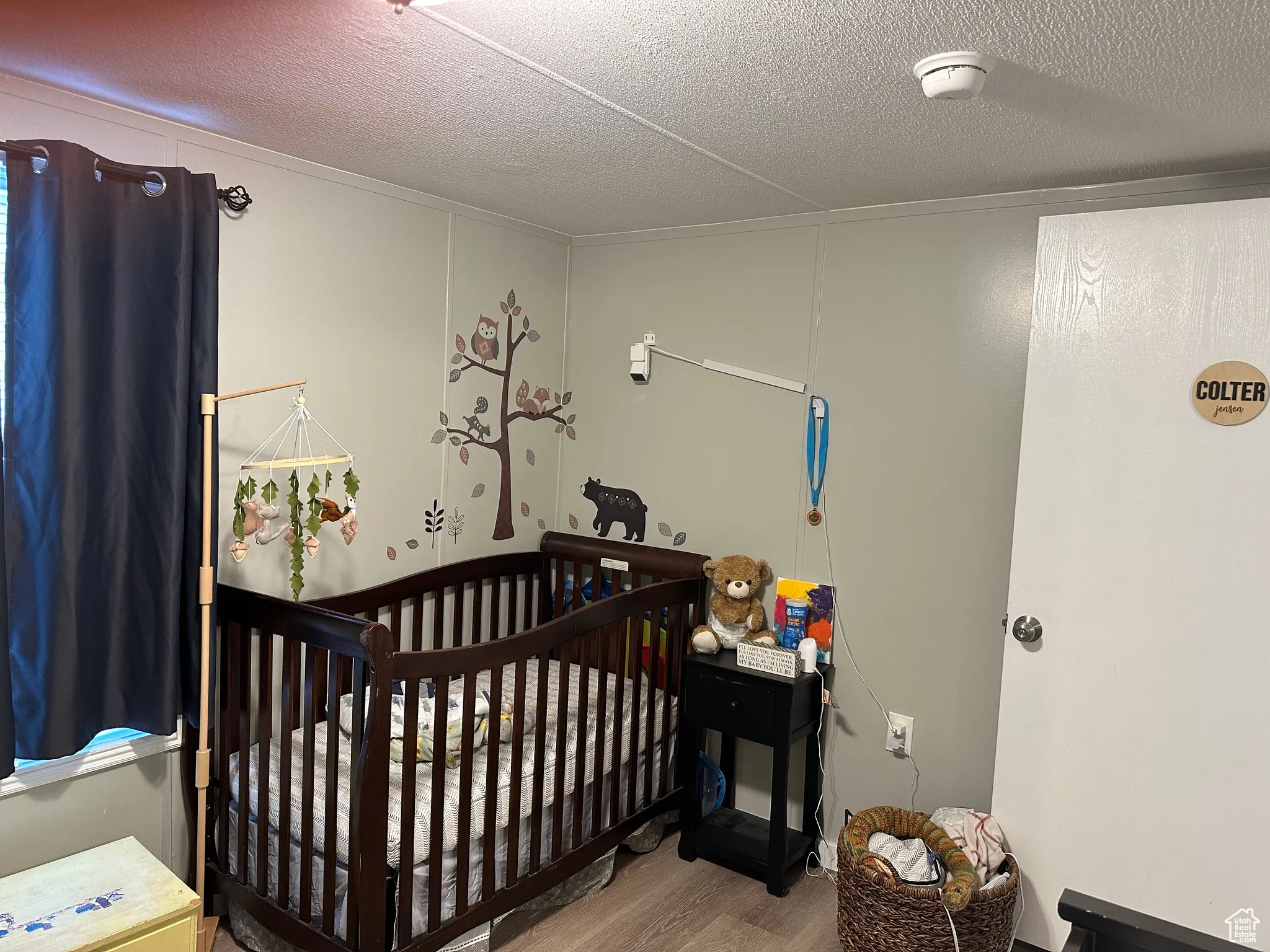 Bedroom with a textured ceiling, light wood-style floors, and a crib