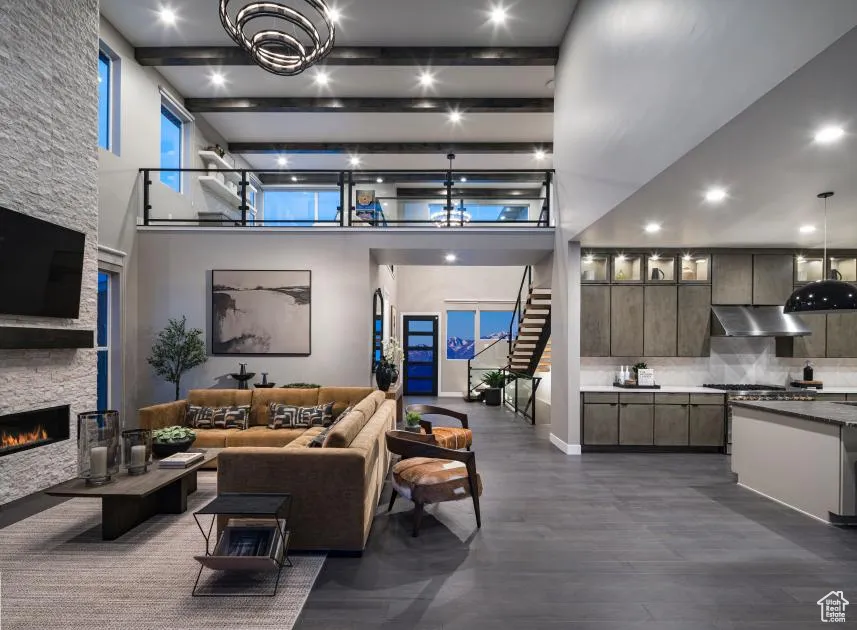 Living area featuring stairway, a stone fireplace, beam ceiling, a towering ceiling, and dark wood-style floors