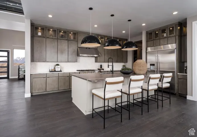 Kitchen with stainless steel built in fridge, glass insert cabinets, a kitchen bar, under cabinet range hood, and hanging light fixtures