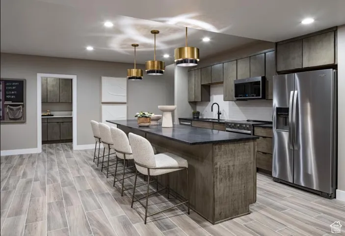 Kitchen featuring appliances with stainless steel finishes, a breakfast bar area, a kitchen island, decorative light fixtures, and wood finish floors