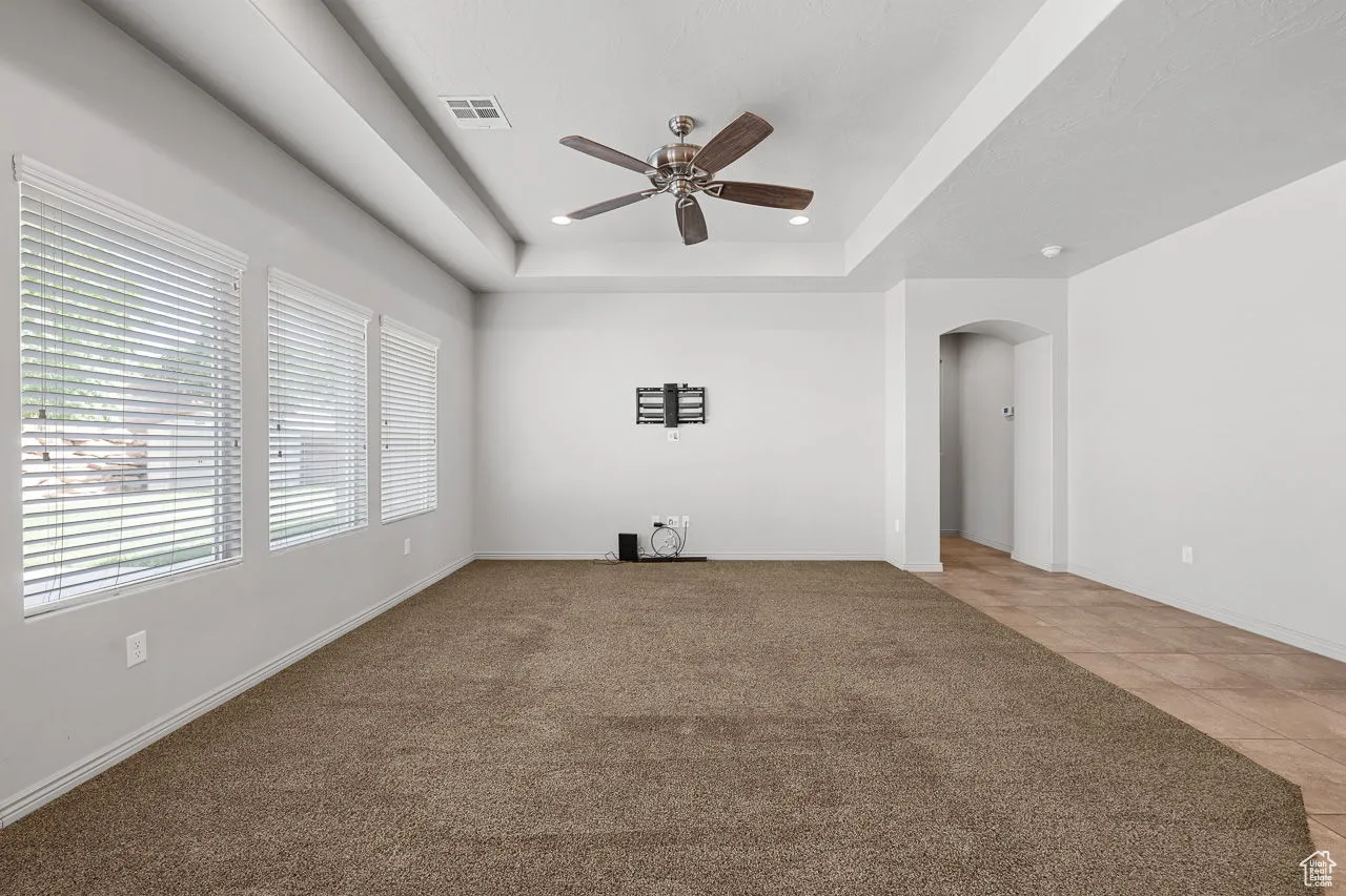 Unfurnished living room featuring arched walkways, a tray ceiling, light colored carpet, ceiling fan, and light tile patterned floors