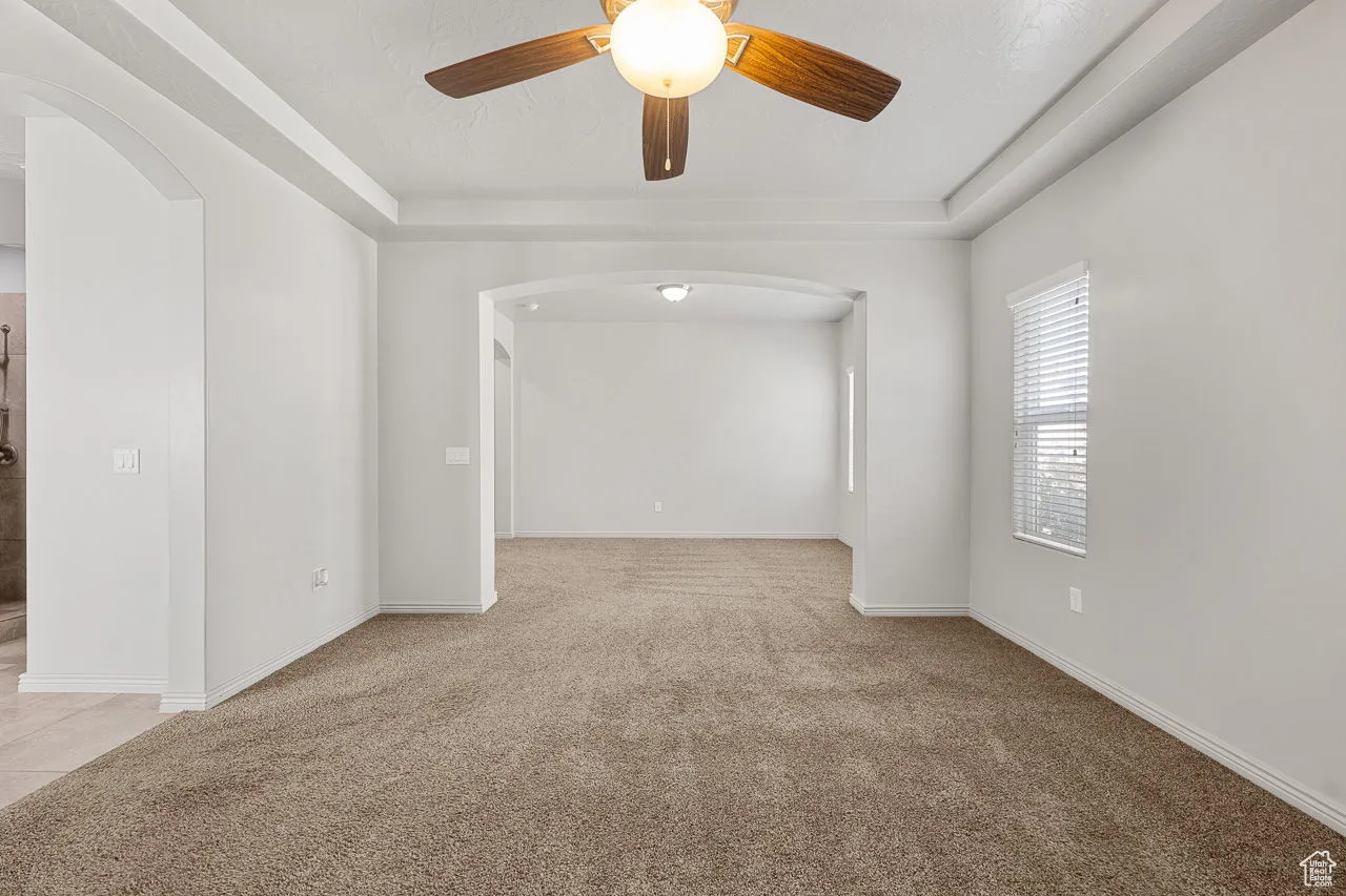 Unfurnished room featuring light carpet, arched walkways, a raised ceiling, and ceiling fan
