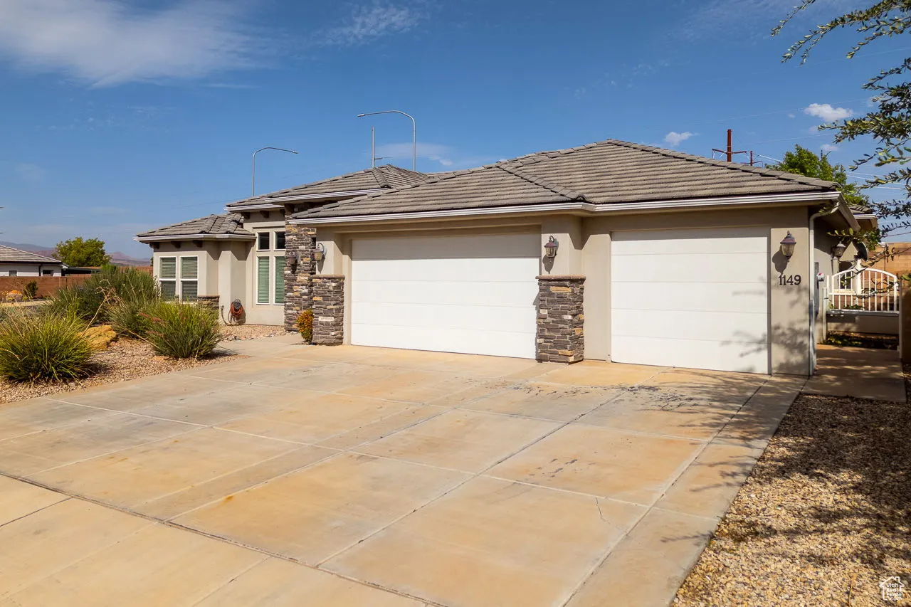 View of front of house with an attached garage, driveway, stucco siding, a tiled roof, and stone siding