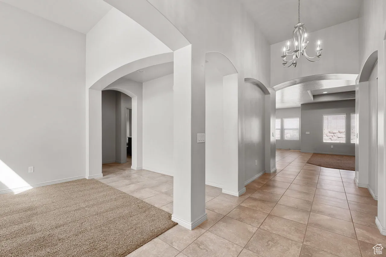 Hallway with a chandelier, light tile patterned floors, arched walkways, and a towering ceiling