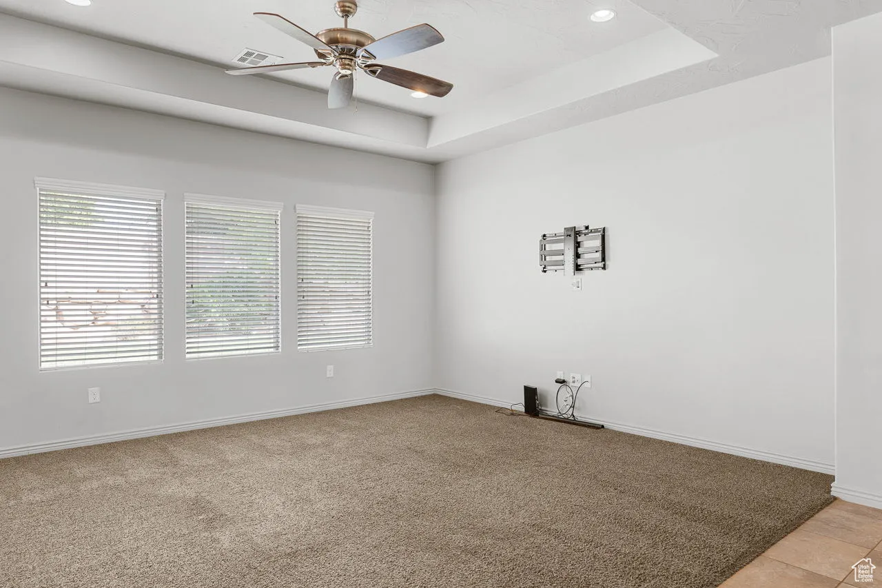 Empty room featuring a tray ceiling, light carpet, recessed lighting, and a ceiling fan