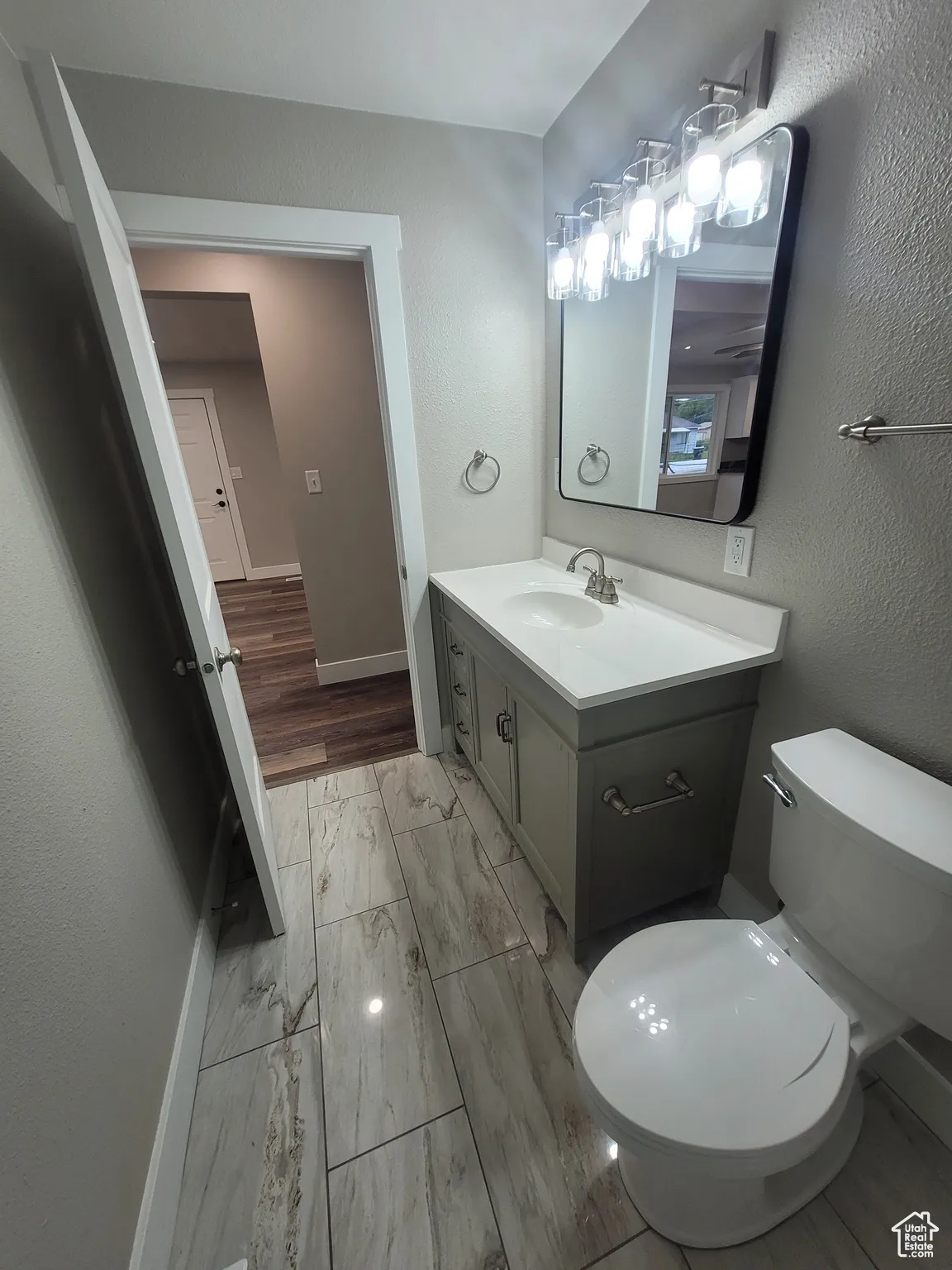 Half bath with vanity, a textured wall, and light marble finish flooring