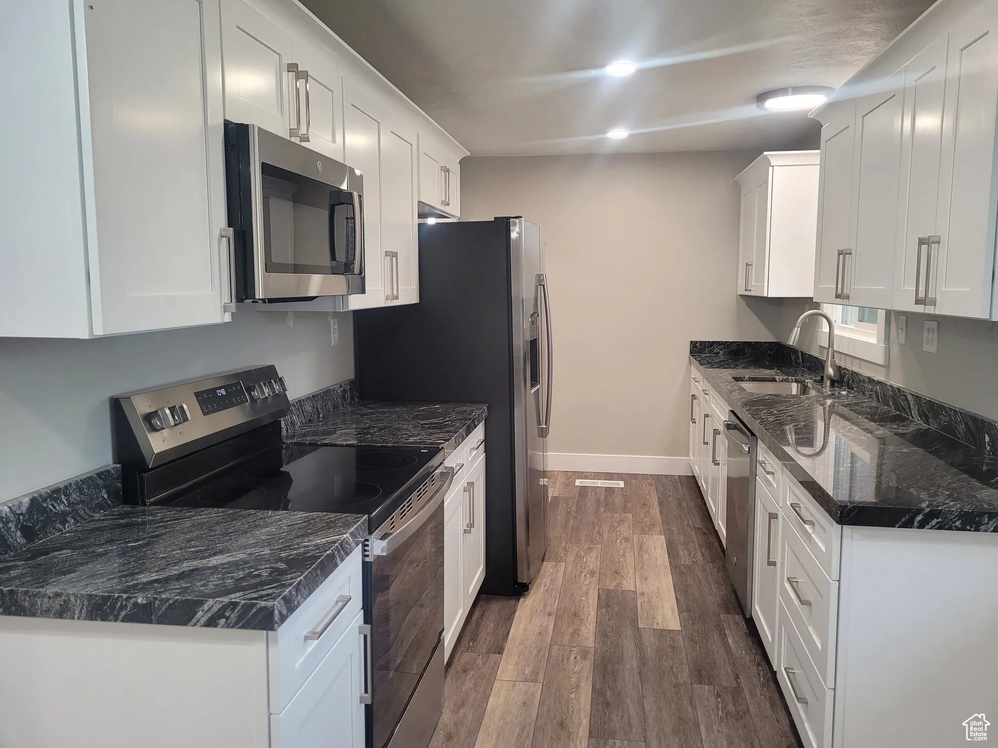 Kitchen with appliances with stainless steel finishes, dark wood-type flooring, white cabinets, dark stone counters, and recessed lighting
