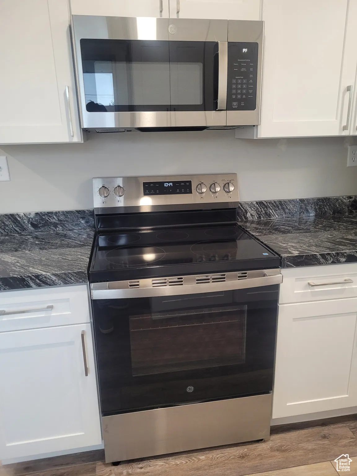 Kitchen with appliances with stainless steel finishes, white cabinets, dark stone countertops, and light wood-style flooring