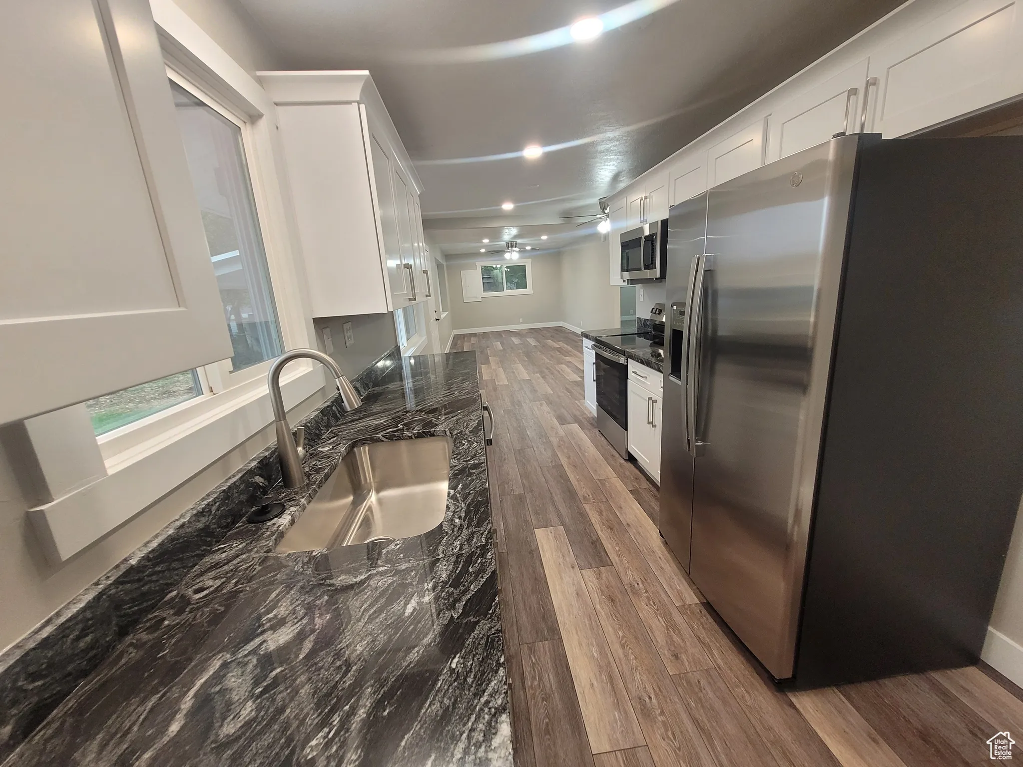 Kitchen with stainless steel appliances, dark stone countertops, white cabinetry, and dark wood-style flooring