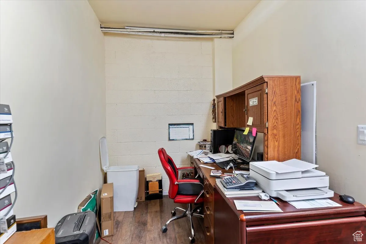 Home office featuring concrete block wall and dark wood-style floors