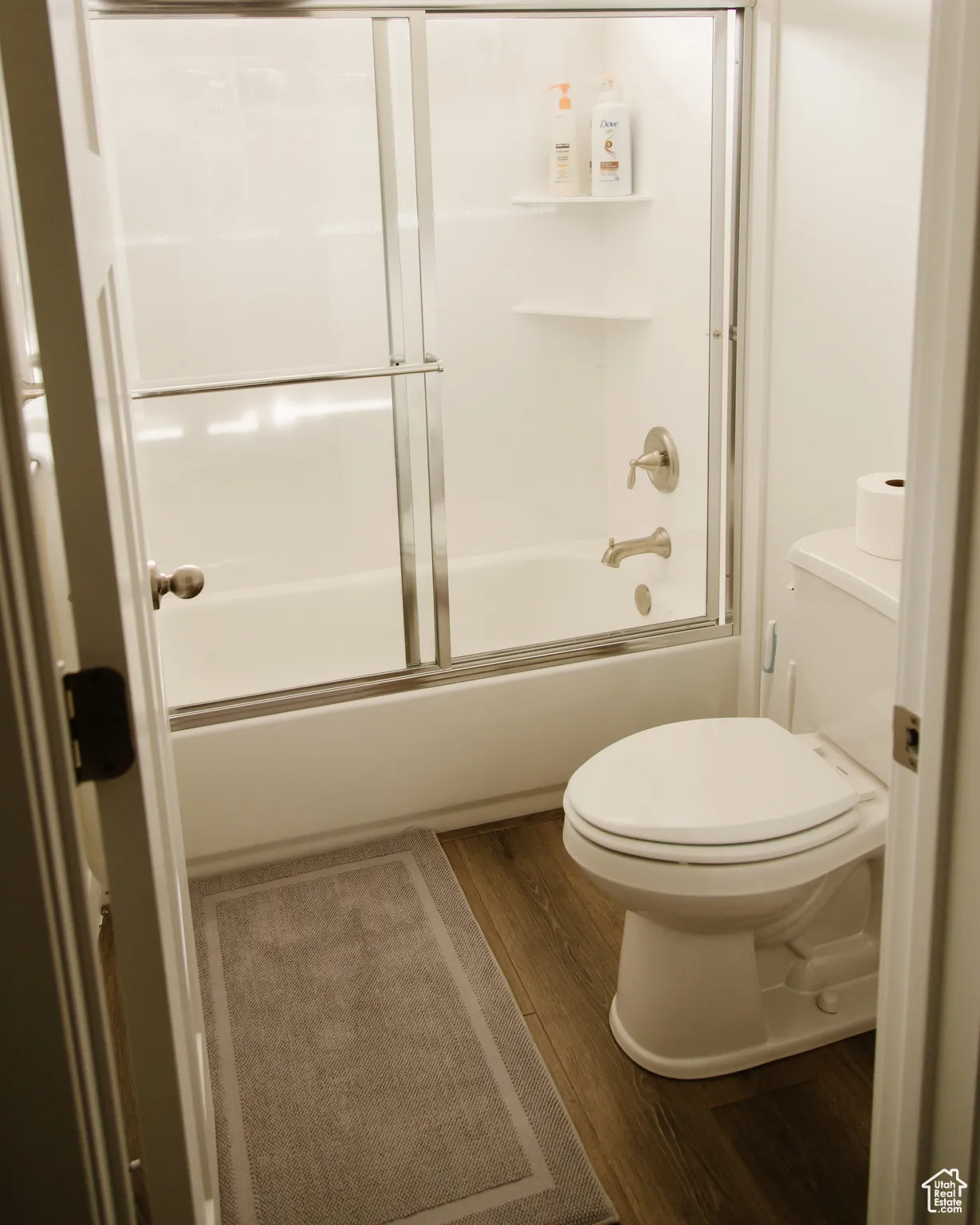 Bathroom with dark wood-type flooring and enclosed tub / shower combo
