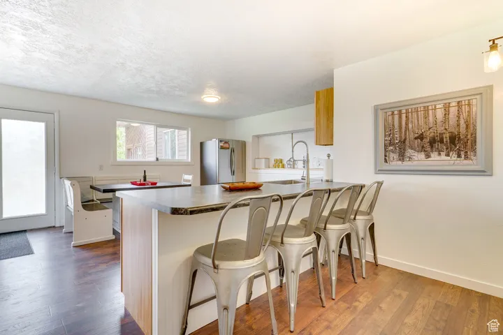 Kitchen with a peninsula, a kitchen bar, freestanding refrigerator, dark wood-style flooring, and dark countertops