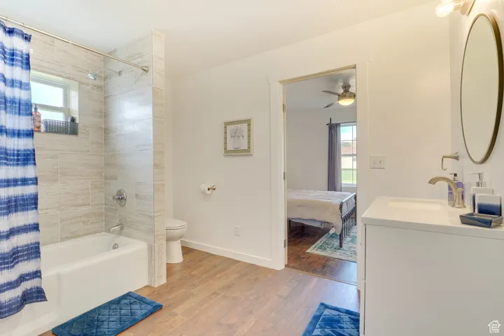 Ensuite bathroom with plenty of natural light, shower / tub combo with curtain, wood finished floors, and vanity