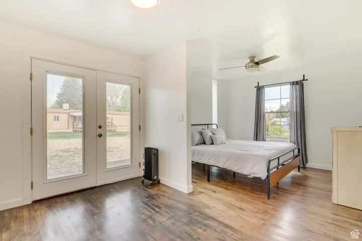 Bedroom with wood finished floors, access to outside, radiator heating unit, ceiling fan, and french doors