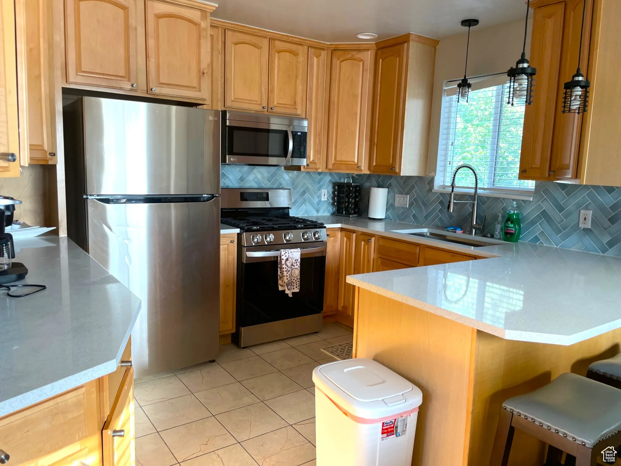 Kitchen featuring appliances with stainless steel finishes, light tile patterned floors, tasteful backsplash, a peninsula, and light stone countertops