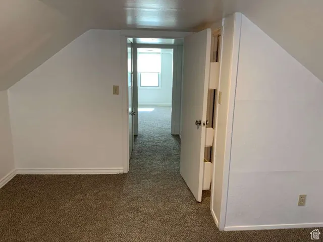 Additional living space featuring dark colored carpet and lofted ceiling