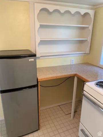 Kitchen featuring built in study area, freestanding refrigerator, light countertops, and white range with electric stovetop
