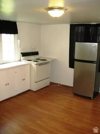 Kitchen with white range with electric cooktop, freestanding refrigerator, dark wood-style flooring, white cabinetry, and light countertops