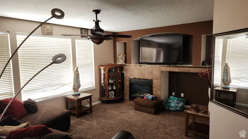 Living area featuring a fireplace, a textured ceiling, dark carpet, and a ceiling fan