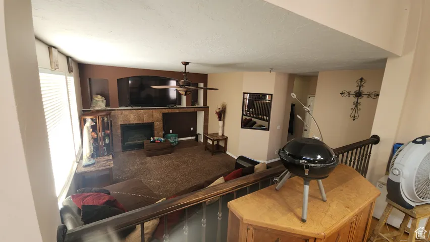 Living room with a textured ceiling, a fireplace, carpet, and a ceiling fan