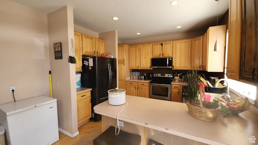 Kitchen featuring a peninsula, stainless steel appliances, light wood finished floors, recessed lighting, and light countertops