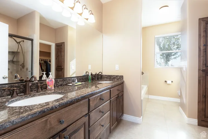 Full bath featuring double vanity, a spacious closet, a bath, a shower stall, and light tile patterned floors