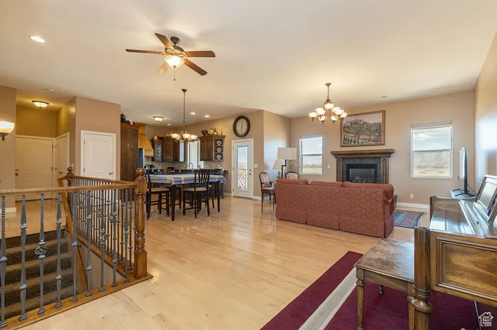 Living room with a chandelier, light wood-type flooring, a glass covered fireplace, a ceiling fan, and recessed lighting