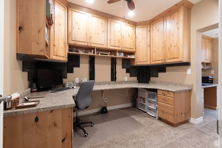 Office with built in study area, light carpet, and a ceiling fan