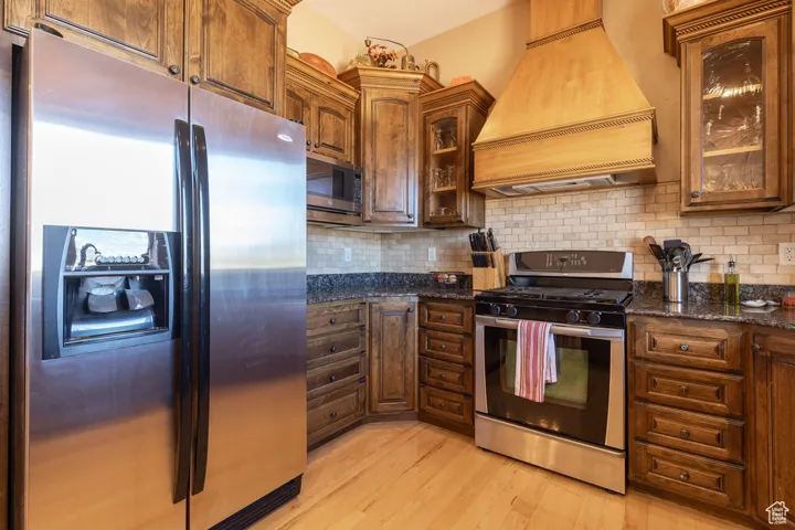 Kitchen with stainless steel appliances, dark stone countertops, custom exhaust hood, and backsplash