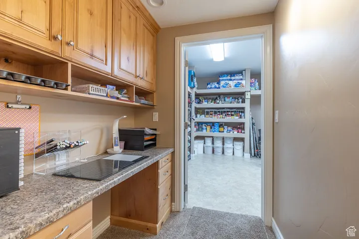 Kitchen featuring built in desk, open shelves, light stone countertops, and brown cabinetry