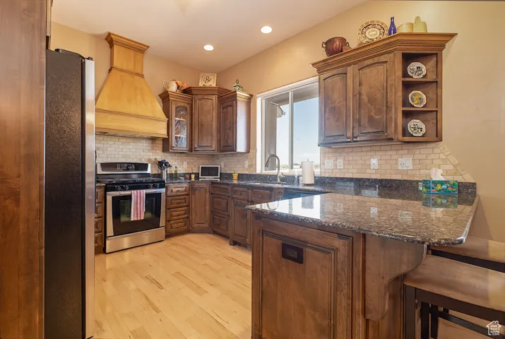 Kitchen featuring appliances with stainless steel finishes, dark stone counters, a peninsula, backsplash, and light wood-style floors