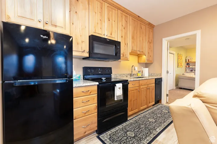 Kitchen featuring black appliances, light stone countertops, and light brown cabinetry