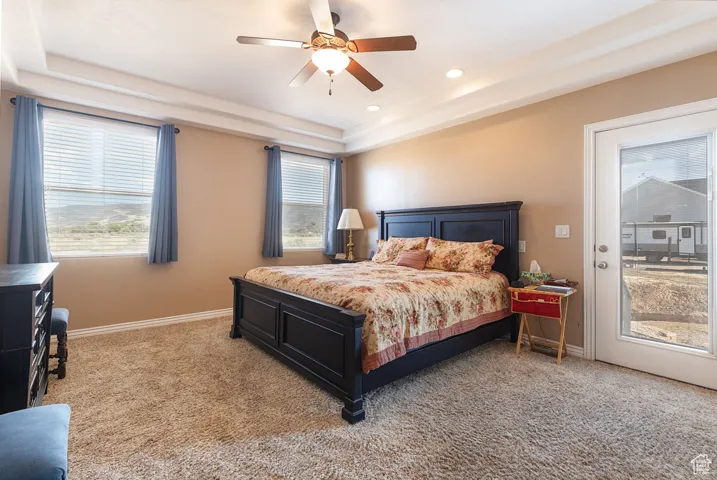 Bedroom with light carpet, a raised ceiling, access to exterior, a ceiling fan, and recessed lighting