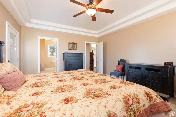 Bedroom with a raised ceiling, a ceiling fan, and carpet flooring