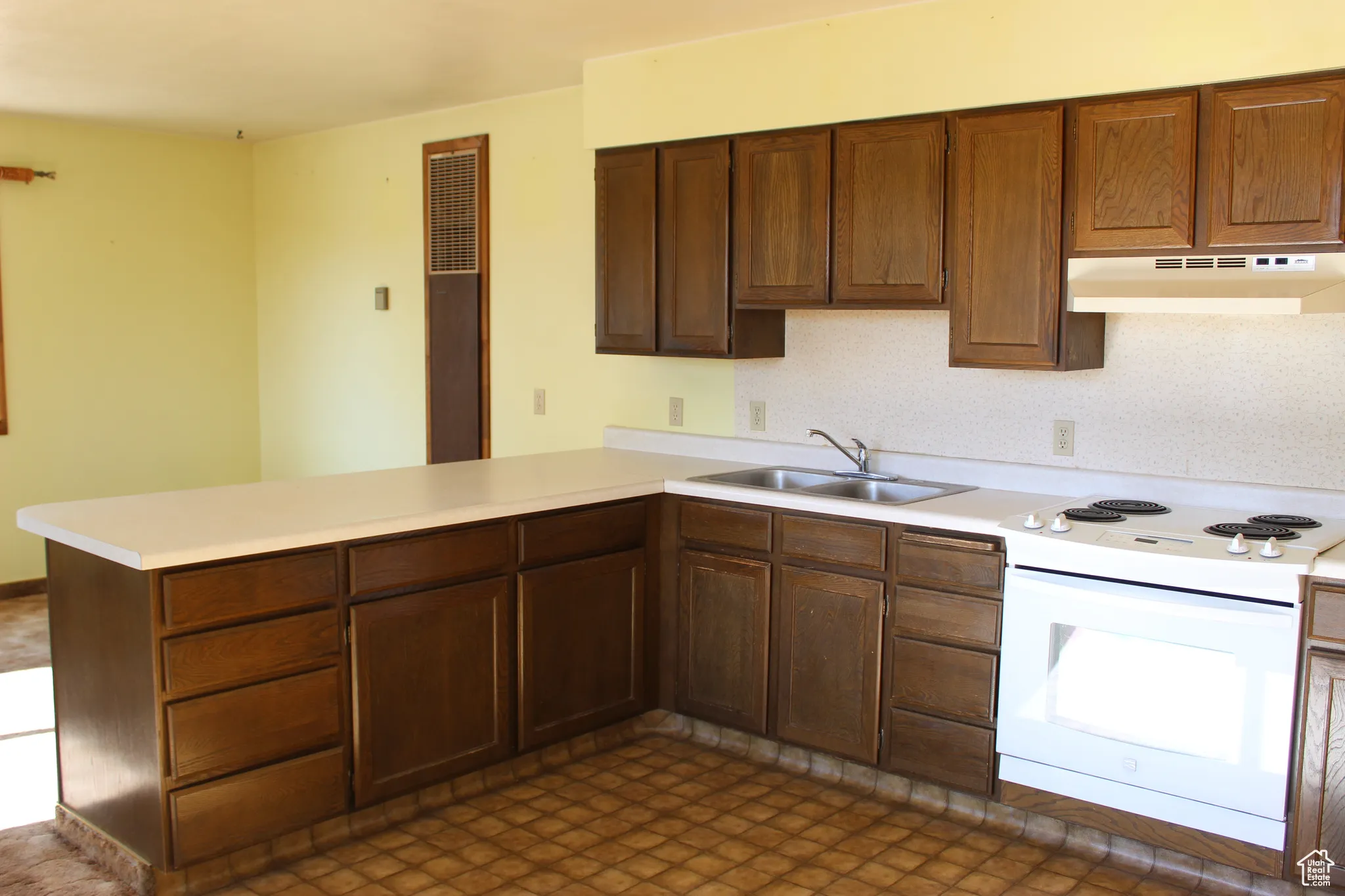 Kitchen featuring electric stove, a peninsula, light countertops, and under cabinet range hood