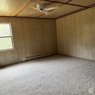 Empty room featuring wood ceiling, a baseboard radiator, wooden walls, and light carpet