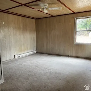 Unfurnished room featuring light carpet, a baseboard radiator, ceiling fan, wooden walls, and wooden ceiling