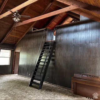 Stairway featuring a wood ceiling with exposed beams, wood walls, ceiling fan, and high vaulted ceiling