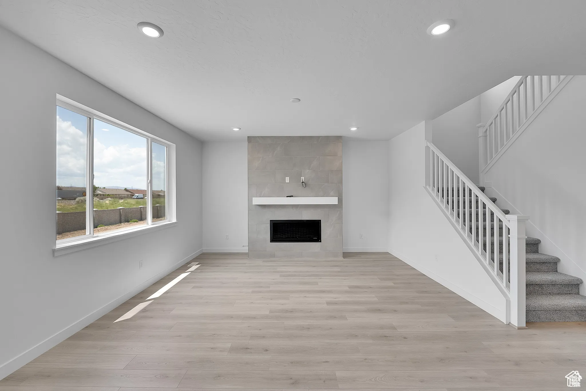 Unfurnished living room with a tile fireplace, stairs, light wood-style floors, and recessed lighting