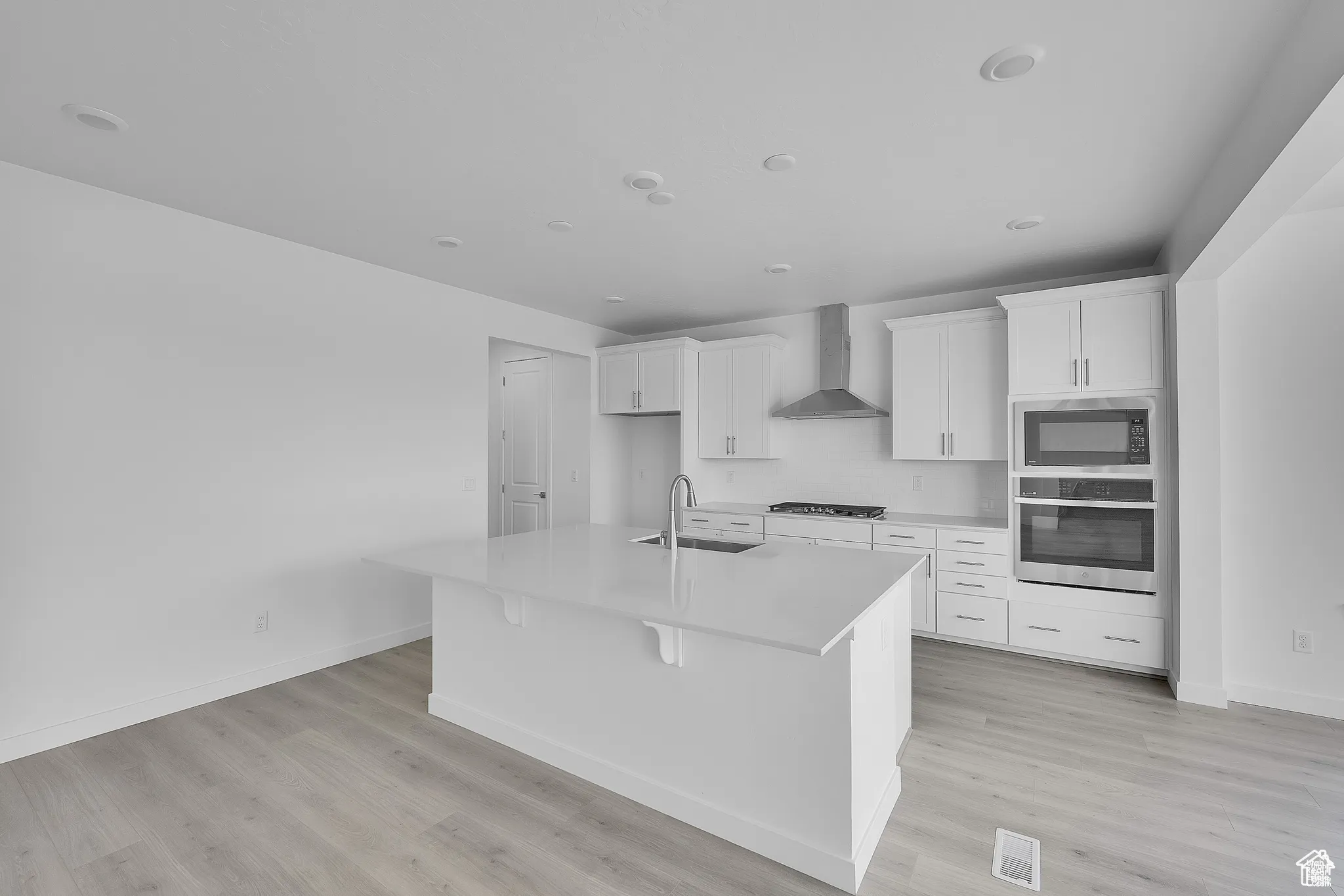 Kitchen featuring black appliances, white cabinets, a center island with sink, light wood-style floors, and wall chimney range hood