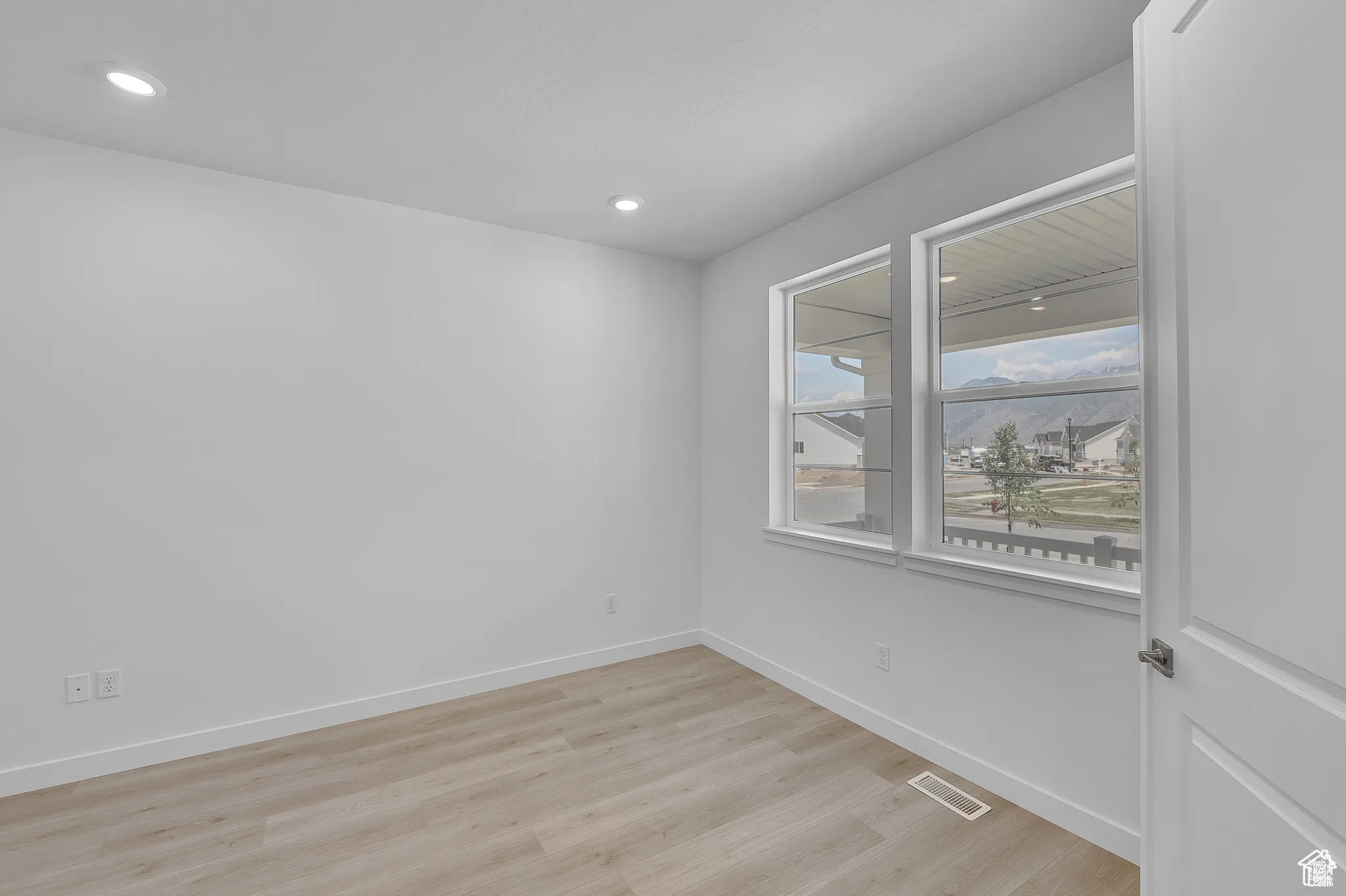 Empty room with light wood-style floors and recessed lighting