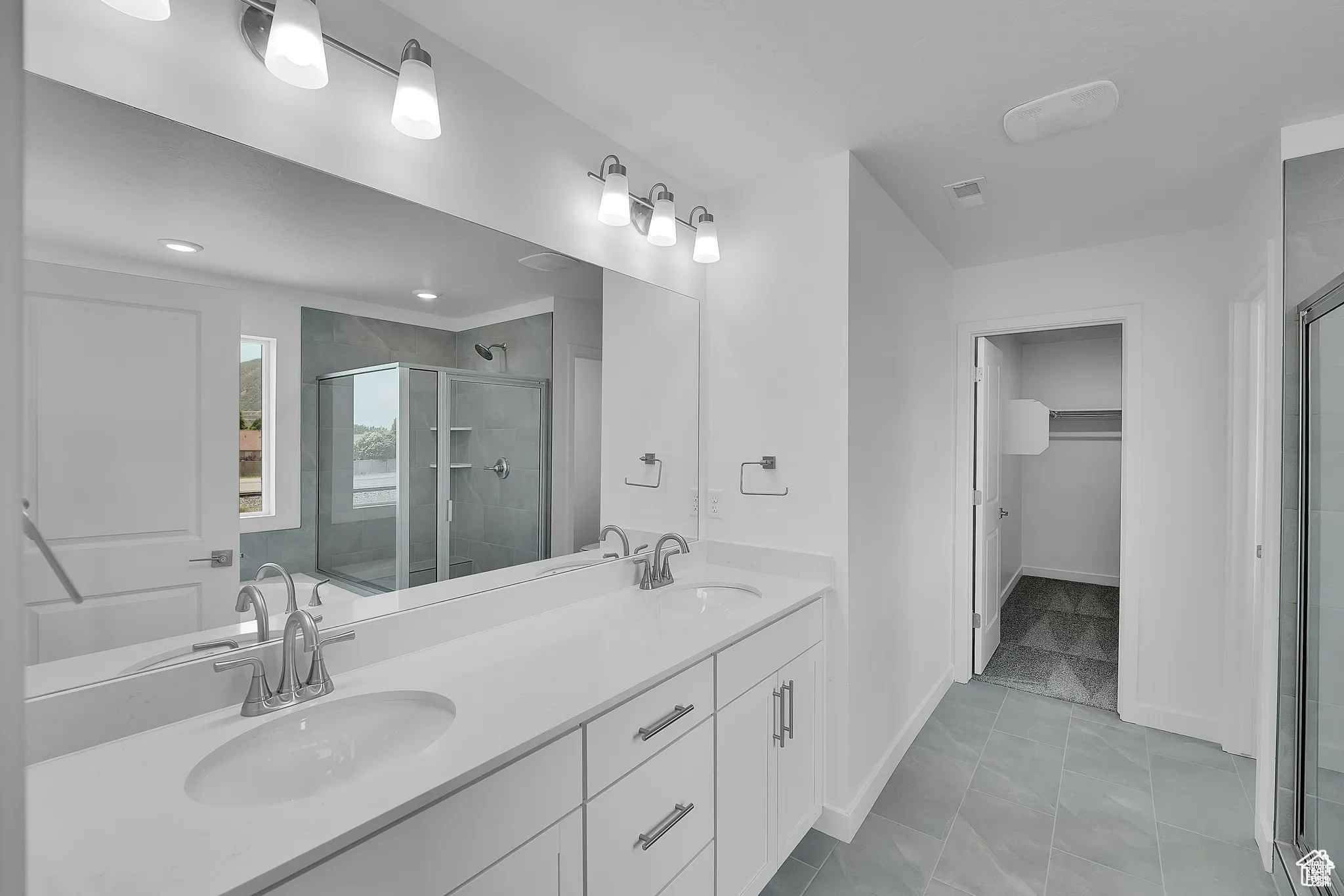 Bathroom featuring a shower stall, double vanity, light tile patterned floors, and a spacious closet