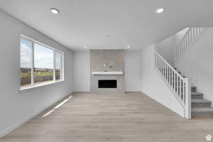 Unfurnished living room with a tile fireplace, stairs, light wood-style floors, and recessed lighting